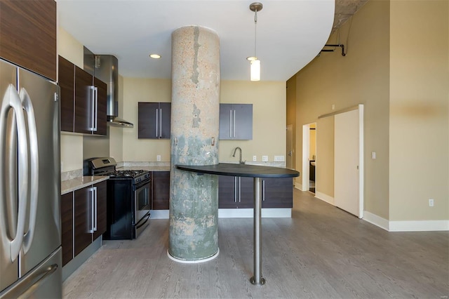 kitchen featuring a breakfast bar, hanging light fixtures, stainless steel appliances, dark brown cabinetry, and light wood-type flooring