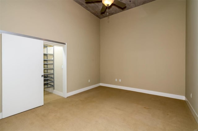 unfurnished room featuring ceiling fan, a towering ceiling, and carpet