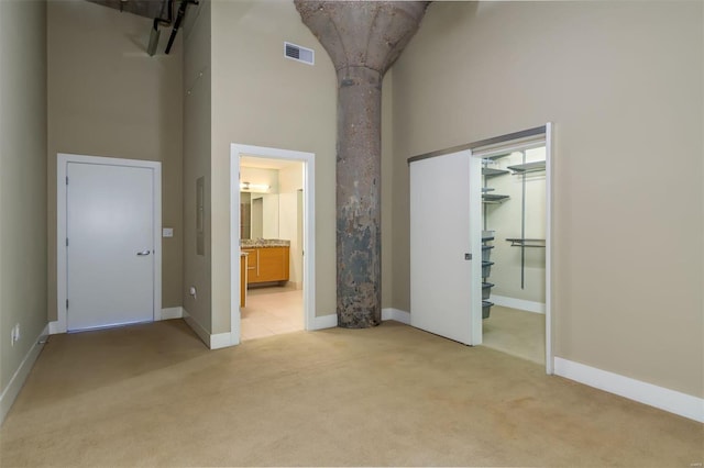 unfurnished bedroom with connected bathroom, light colored carpet, high vaulted ceiling, and a closet