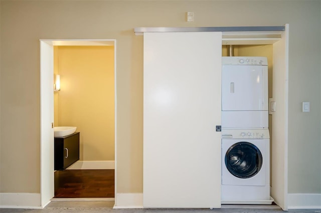 washroom featuring stacked washer / drying machine, baseboards, wood finished floors, and laundry area