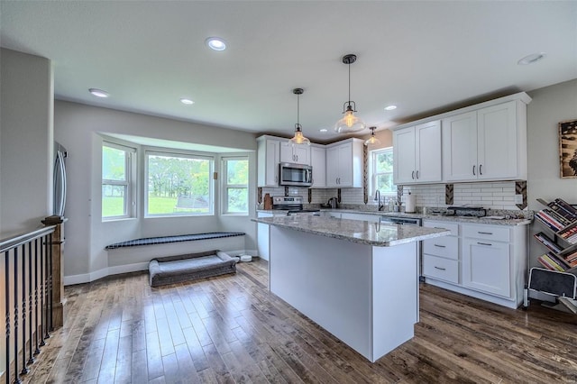 kitchen featuring appliances with stainless steel finishes, white cabinetry, decorative light fixtures, and dark hardwood / wood-style floors