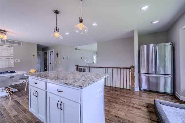 kitchen with hanging light fixtures, white cabinetry, light stone counters, stainless steel refrigerator, and dark hardwood / wood-style floors