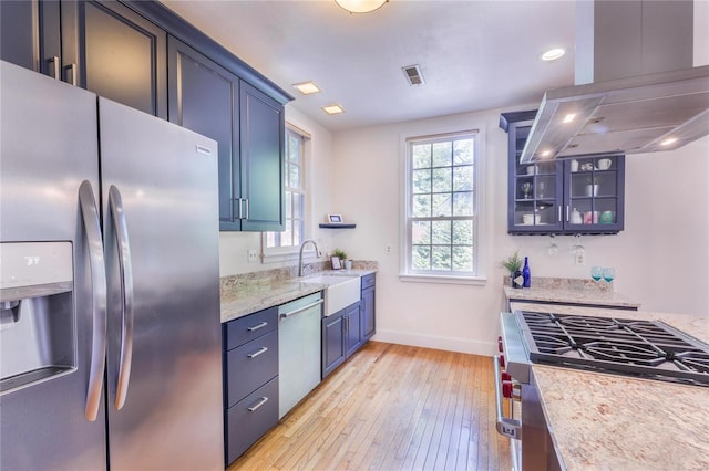 kitchen with appliances with stainless steel finishes, light hardwood / wood-style flooring, sink, light stone countertops, and island exhaust hood