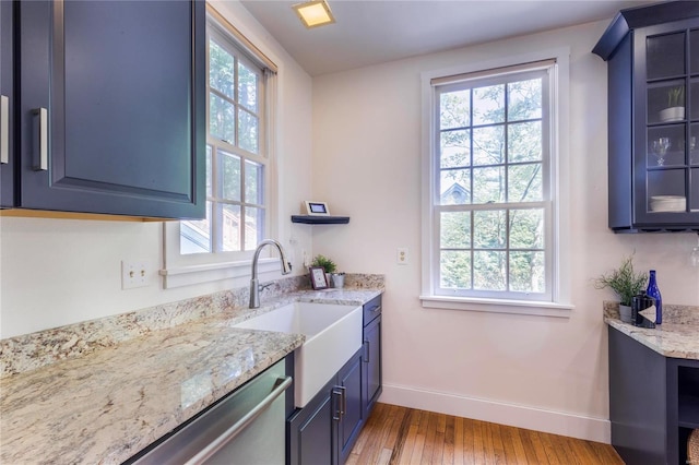 kitchen featuring light stone counters, stainless steel dishwasher, blue cabinetry, hardwood / wood-style flooring, and sink