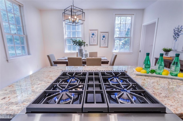 interior space featuring a healthy amount of sunlight, stainless steel gas cooktop, light stone counters, and a chandelier