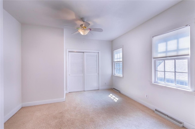 unfurnished bedroom with a baseboard radiator, multiple windows, light colored carpet, and ceiling fan