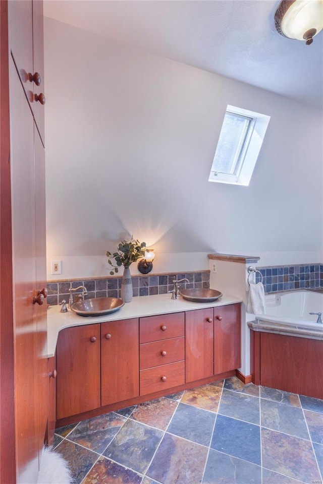 bathroom with vaulted ceiling with skylight, a bathtub, backsplash, tile patterned floors, and double sink vanity