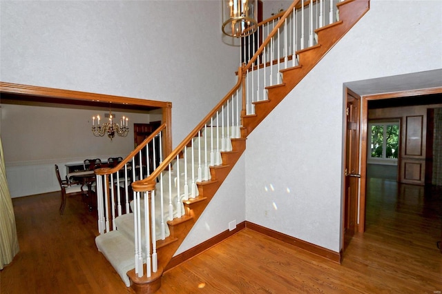 stairway with hardwood / wood-style flooring, a towering ceiling, and an inviting chandelier