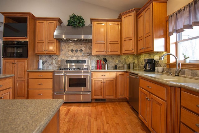 kitchen with decorative backsplash, appliances with stainless steel finishes, wall chimney exhaust hood, sink, and light hardwood / wood-style flooring