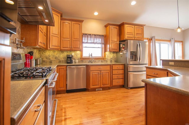 kitchen with sink, hanging light fixtures, extractor fan, appliances with stainless steel finishes, and light wood-type flooring