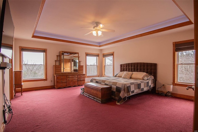 carpeted bedroom with a tray ceiling, multiple windows, and ceiling fan