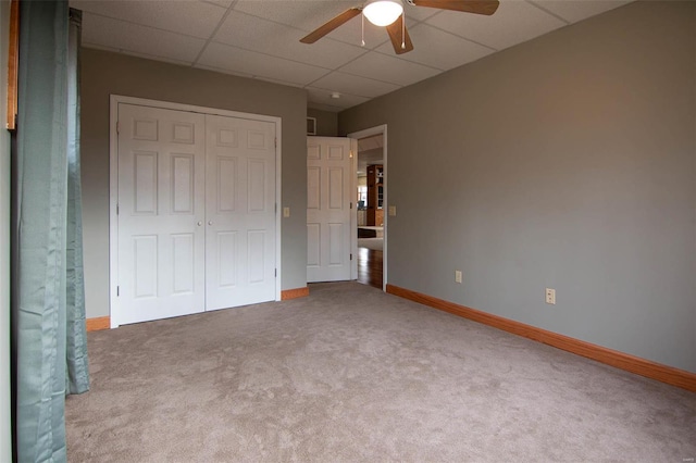 unfurnished bedroom featuring carpet, a drop ceiling, a closet, and ceiling fan