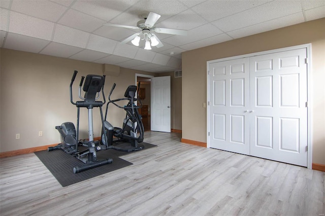 exercise room featuring light wood-type flooring, ceiling fan, and a paneled ceiling