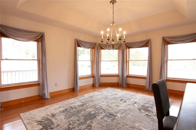 unfurnished dining area with baseboards, a tray ceiling, an inviting chandelier, and wood finished floors