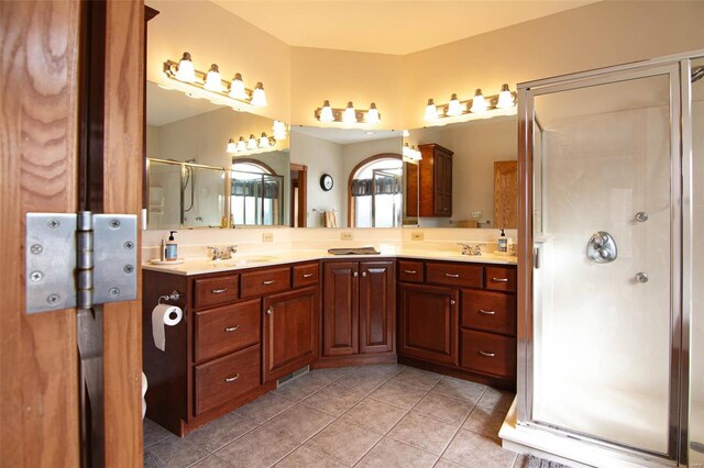 bathroom featuring tile patterned flooring, a sink, a stall shower, and double vanity