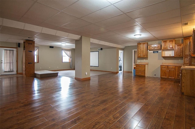unfurnished living room featuring baseboards, dark wood-style flooring, and a drop ceiling