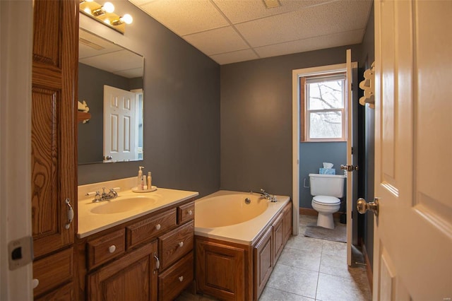 bathroom with a bath, vanity, tile patterned floors, toilet, and a drop ceiling
