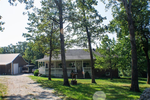 single story home with a detached garage, a porch, a front yard, an outbuilding, and driveway