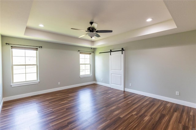 unfurnished room featuring hardwood / wood-style floors, ceiling fan, a raised ceiling, and a barn door