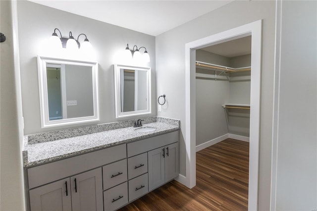 bathroom with a walk in closet, wood finished floors, vanity, and baseboards