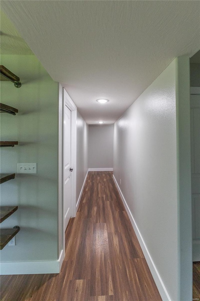 corridor featuring baseboards, wood finished floors, and a textured ceiling