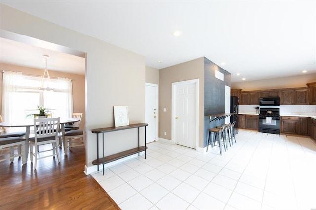 kitchen featuring pendant lighting, an inviting chandelier, backsplash, dark brown cabinetry, and black appliances