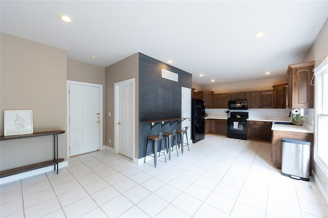 kitchen featuring dark brown cabinets, light tile patterned floors, decorative backsplash, and black appliances