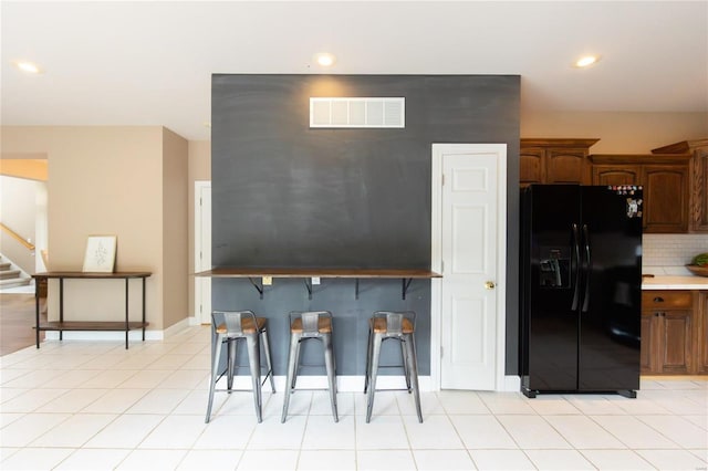 kitchen with black fridge, a kitchen breakfast bar, tasteful backsplash, and light tile patterned floors