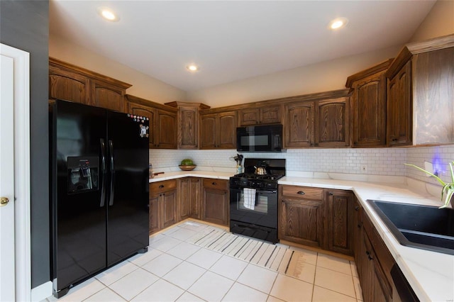 kitchen featuring sink, light tile patterned floors, dark brown cabinetry, black appliances, and decorative backsplash