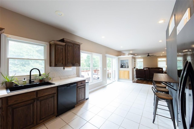 kitchen featuring sink, dishwasher, backsplash, dark brown cabinetry, and a wealth of natural light