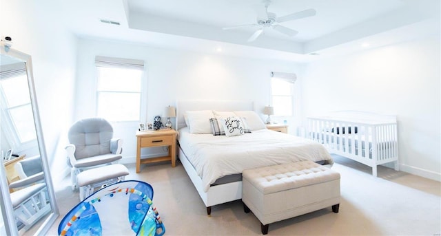 carpeted bedroom with ceiling fan and a tray ceiling