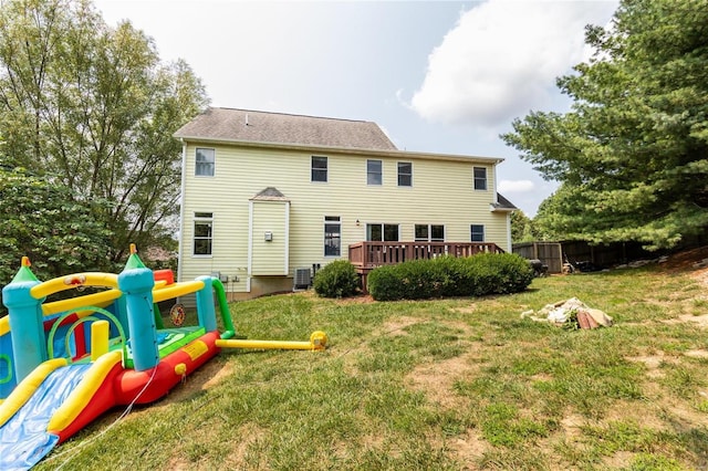 rear view of property featuring central AC unit, a playground, a deck, and a lawn