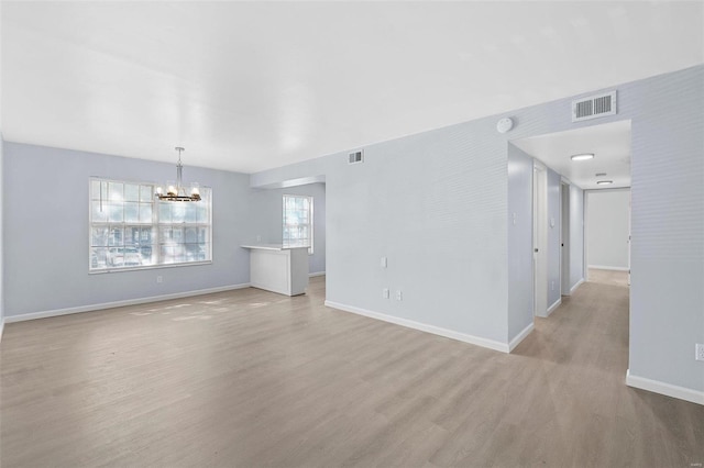 unfurnished living room with an inviting chandelier and light wood-type flooring