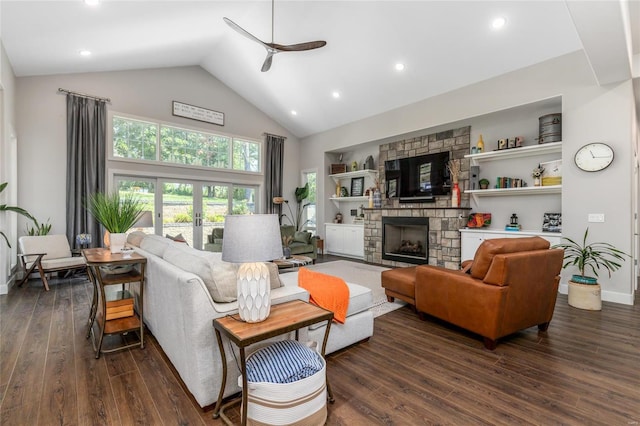 living room featuring ceiling fan, built in shelves, dark hardwood / wood-style flooring, and a stone fireplace