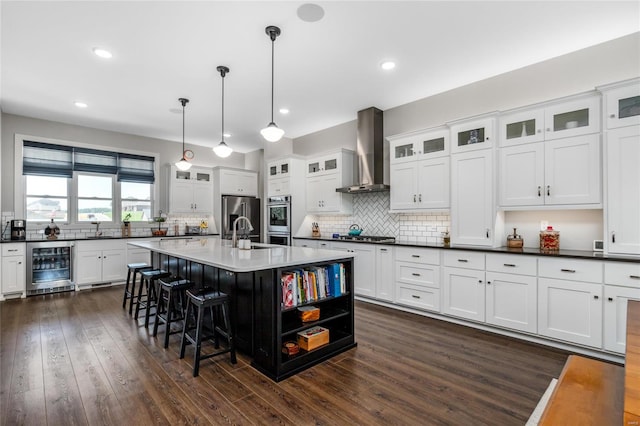 kitchen featuring wall chimney range hood, hanging light fixtures, beverage cooler, stainless steel appliances, and dark hardwood / wood-style flooring