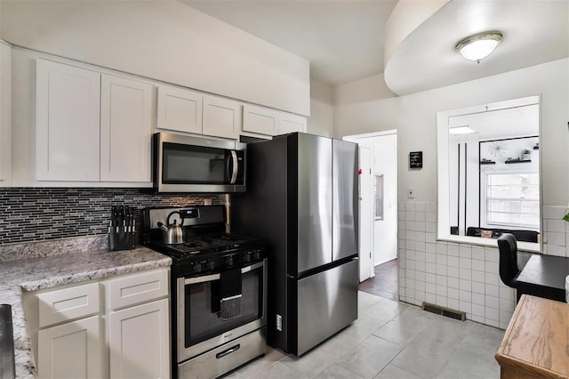 kitchen featuring stainless steel appliances, light tile patterned flooring, tile walls, white cabinets, and light stone counters