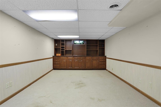 basement with a paneled ceiling, light colored carpet, and built in shelves