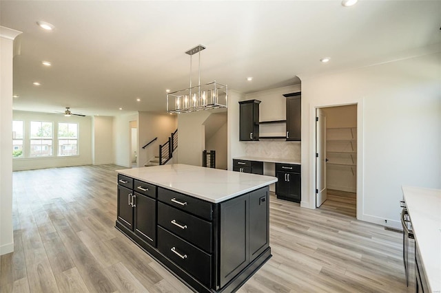 kitchen with a kitchen island, hanging light fixtures, backsplash, and light hardwood / wood-style flooring