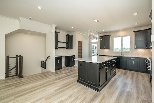 kitchen with light wood-type flooring, a kitchen island, sink, decorative backsplash, and pendant lighting