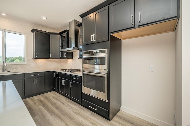 kitchen with appliances with stainless steel finishes, wall chimney exhaust hood, light stone counters, decorative backsplash, and sink