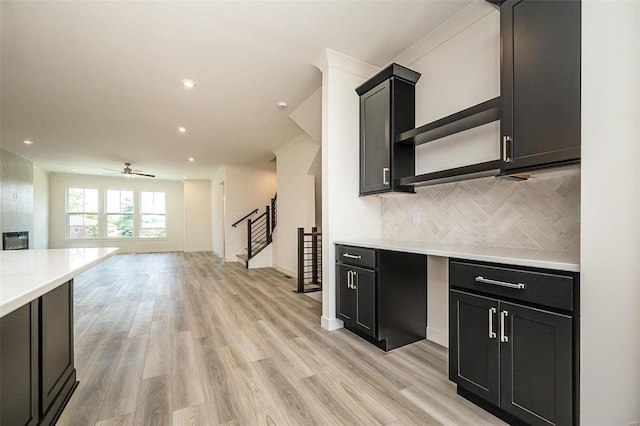 kitchen featuring ceiling fan, a tiled fireplace, decorative backsplash, and light hardwood / wood-style flooring