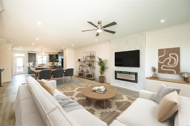 living room featuring light wood-type flooring, ceiling fan, and a fireplace