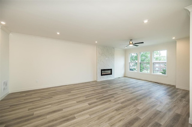 unfurnished living room with ceiling fan, light hardwood / wood-style flooring, a premium fireplace, and crown molding