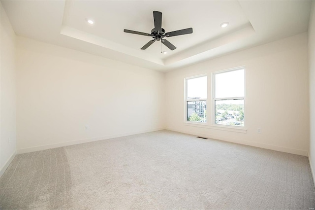 carpeted spare room with ceiling fan and a raised ceiling