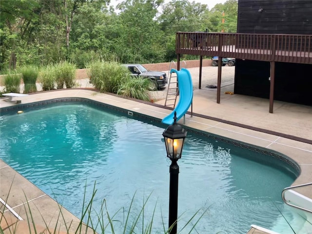 outdoor pool with a diving board, a patio, a water slide, and a wooden deck