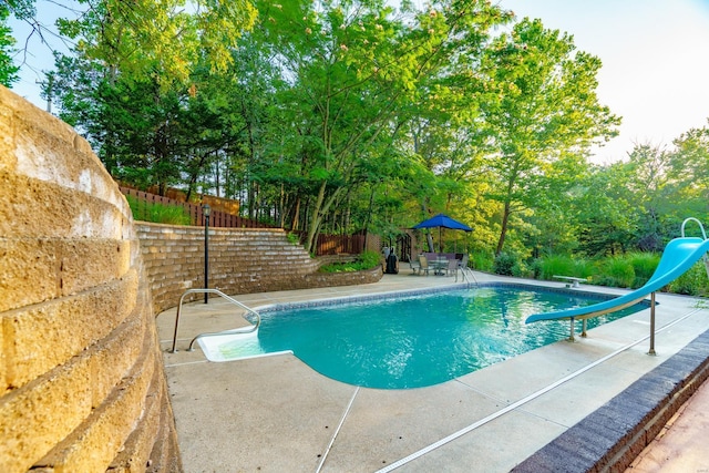 outdoor pool with a diving board, a water slide, a patio, and fence