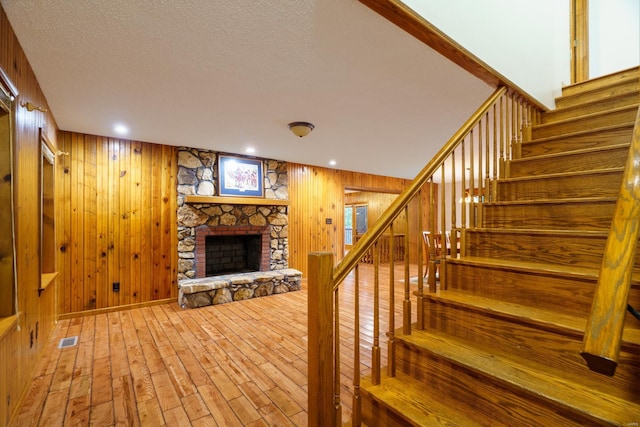 staircase featuring visible vents, wood walls, a stone fireplace, a textured ceiling, and wood finished floors