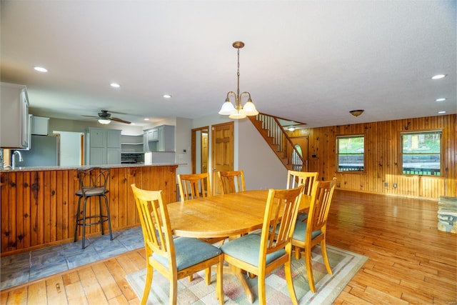 dining room featuring recessed lighting, stairway, light wood-style floors, wood walls, and ceiling fan with notable chandelier