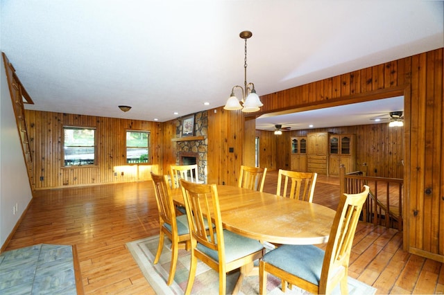 dining room featuring light wood finished floors, wooden walls, baseboards, a ceiling fan, and a fireplace