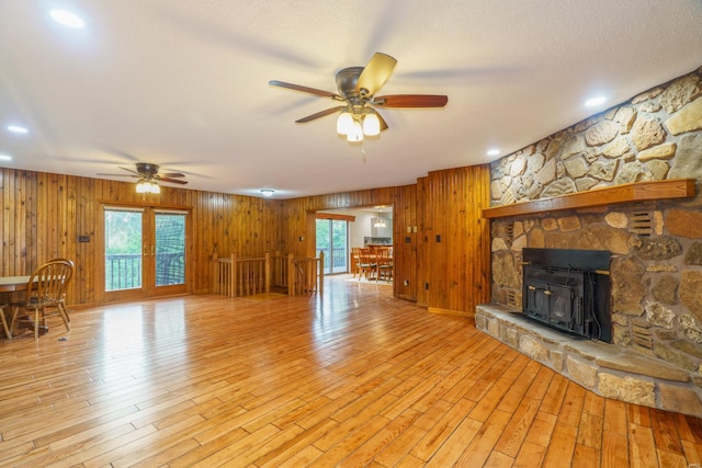 unfurnished living room with light wood-type flooring, wooden walls, a ceiling fan, and a textured ceiling